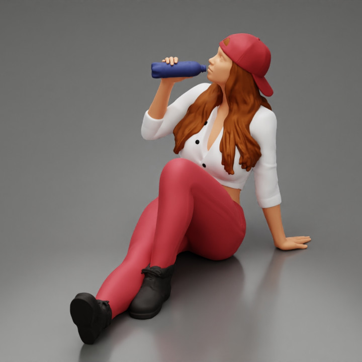 Tired woman mechanic in shirt pants and backwards cap sitting and drinking water during from bottle image