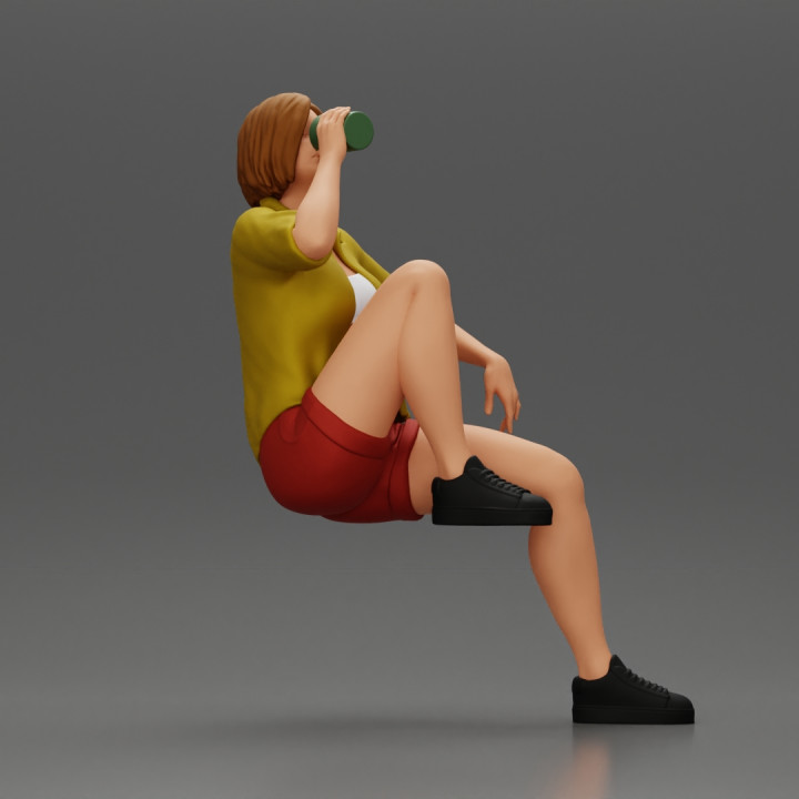 Young woman sitting on a chair hugging her pulled-up leg while drinking image